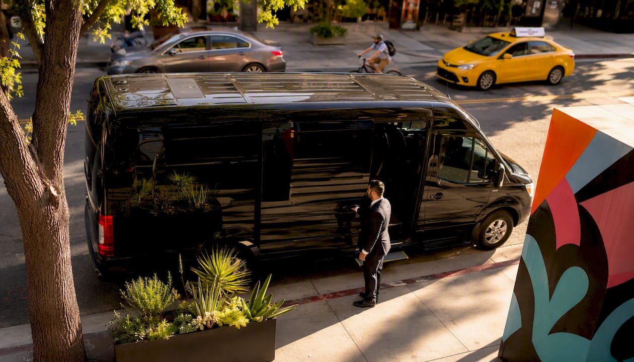 Chauffeur opening branded minivan door on urban street