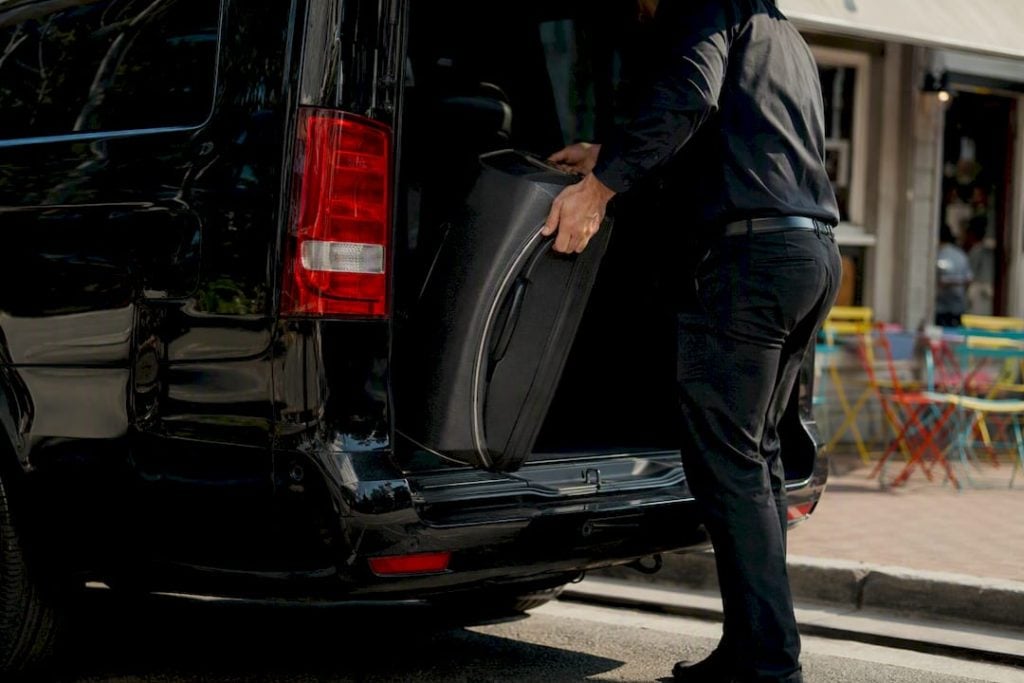 Chauffeur loading luggage into black Sprinter minivan trunk